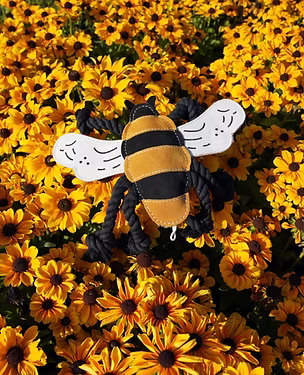 Close-up of Bessie the Bumble Bee toy by Aurora Paws resting amongst bright yellow flowers, supplied by Paw Branch.