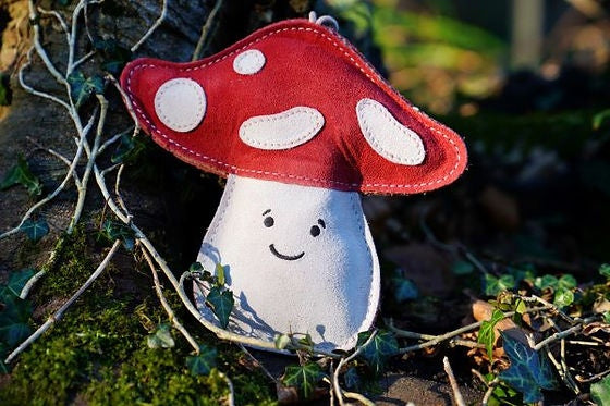Red and white suede Marie the Mushroom dog toy resting on mossy tree bark and ivy, supplied by Paw Branch.